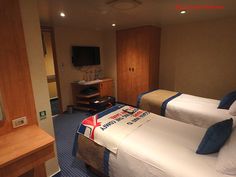 two twin beds in a hotel room with blue carpeting and wooden cabinets, television on the wall