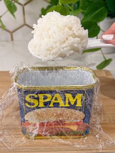 a can of spam sitting on top of a wooden cutting board next to rice