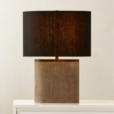 a lamp that is sitting on top of a white table with a brown shade over it