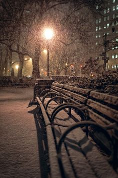 a row of park benches covered in snow next to a street light at night time