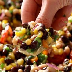 a hand holding a tortilla filled with black eyed peas, corn and tomatoes