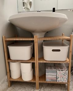 a bathroom sink sitting next to a wooden shelf filled with containers and paper towels on top of it