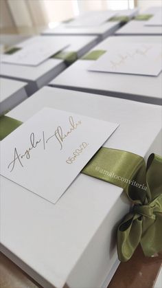 several white boxes with green ribbons and cards on top of each box, all wrapped in satin ribbon