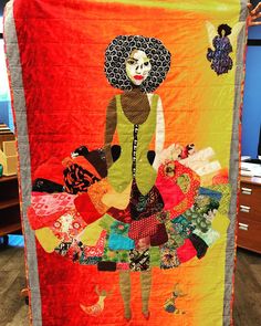 a woman holding up a colorful quilt with an image of a woman in a dress on it