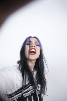 a woman with blue hair and makeup is holding her hands out in front of her face