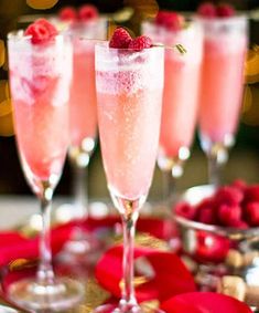 three champagne flutes filled with raspberries and topped with a red rose garnish