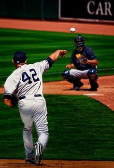 a baseball player throwing a ball on top of a field with another man behind him