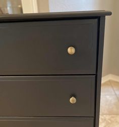 a black dresser with gold handles and knobs on the bottom drawer, in front of a white wall