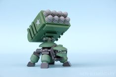 a green toy with lots of balls on it's head and arms, sitting in front of a blue background