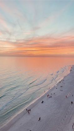 an aerial view of people walking on the beach at sunset or sunrise with pink and blue colors