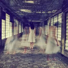 a woman in a white dress is walking through an empty room with windows and shutters