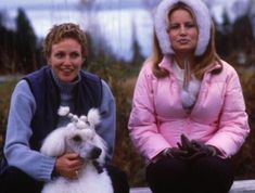 two women sitting on a bench with a small white poodle in front of them