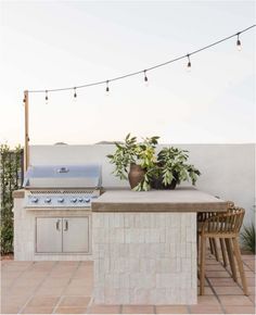 an outdoor kitchen with potted plants on the counter and lights strung above it, along with chairs