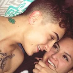 two people laying next to each other with tattoos on their arms and chest, looking at the camera