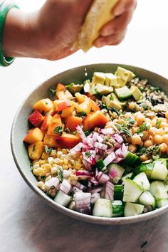 a person is sprinkling dressing on a bowl of food that includes beans, cucumbers, and avocado