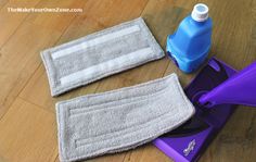 two cleaning cloths sitting on top of a wooden floor next to a blue bottle