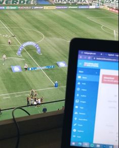 a laptop computer sitting on top of a desk next to a soccer field with players