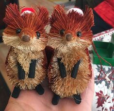 two small toy hedgehogs sitting on top of someone's hand next to a christmas tree