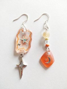 two earrings with charms hanging from them on a white surface, one has a star and the other has a crescent