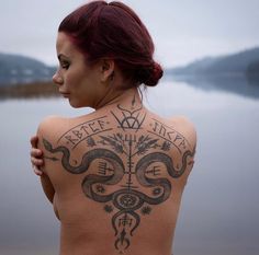 a woman with tattoos on her back standing next to the water and looking off into the distance