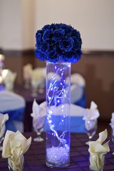 a vase filled with blue roses and lights on top of a table covered in white napkins