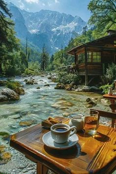 a wooden table sitting next to a river filled with lots of water and mountains in the background