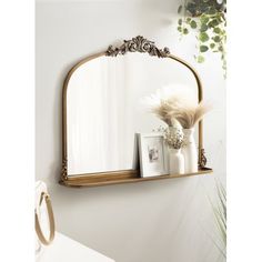 a mirror sitting on top of a wooden shelf next to a vase and potted plant