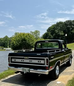 an old black truck parked on the side of a road next to a body of water