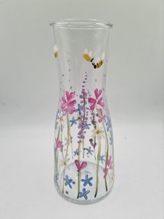 a glass vase with flowers and a bee painted on the side, sitting on a white surface