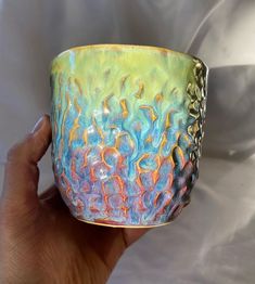 a hand holding a colorful glass cup in front of a white background with gold trim