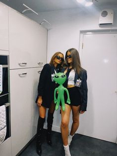 two women standing next to each other in a room with white cupboards and appliances