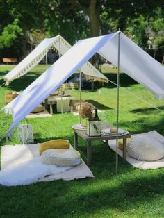 tents set up in the grass with pillows and blankets on them, for an outdoor party