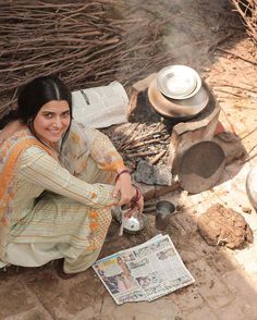 a woman sitting on the ground next to an open fire with pots and pans