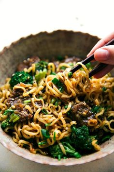 someone holding chopsticks over a bowl of noodles with broccoli and meat