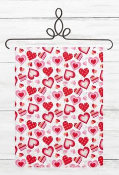 a red and pink heart patterned tea towel hanging on a metal rack with white wood planks