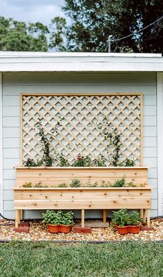 a wooden bench sitting in front of a white shed with potted plants on it