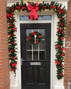 a black door decorated with christmas wreaths and red bows