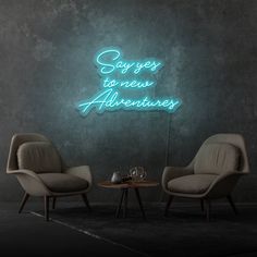 two chairs and a table in front of a neon sign that says sorry to new adventures