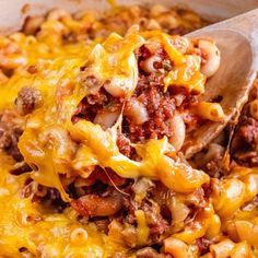 a casserole dish with meat and cheese being lifted by a wooden spatula