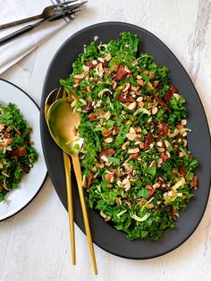 a salad with nuts and greens on a black plate next to a gold spoon, silverware