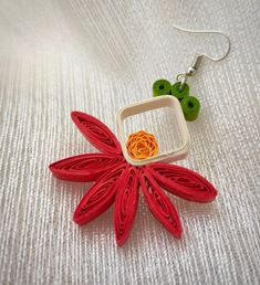 a pair of earrings with red and orange flowers attached to them on a white surface