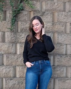 a woman standing in front of a brick wall with her hand on her hip and looking down