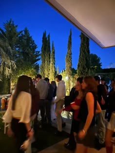 a group of people standing around each other in front of trees and bushes at night