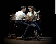 two people sitting on a bench with guitars in their hands and one person playing the guitar