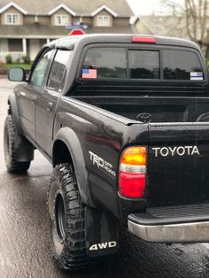 the back end of a black toyota truck parked in front of a house on a rainy day