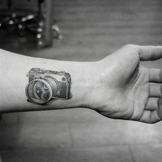 a camera tattoo on the left wrist and right hand is shown in black and white