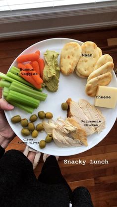 a white plate topped with meat and veggies next to crackers on top of a wooden floor