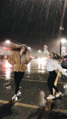 two girls jumping in the rain with their hands up and one girl holding an umbrella