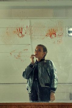 a woman standing in front of a mirror with blood on the wall behind her and holding a cell phone to her ear