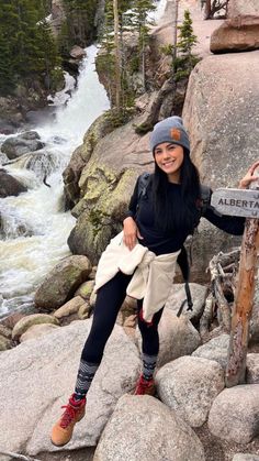 a woman sitting on top of a rock next to a river and holding onto a sign